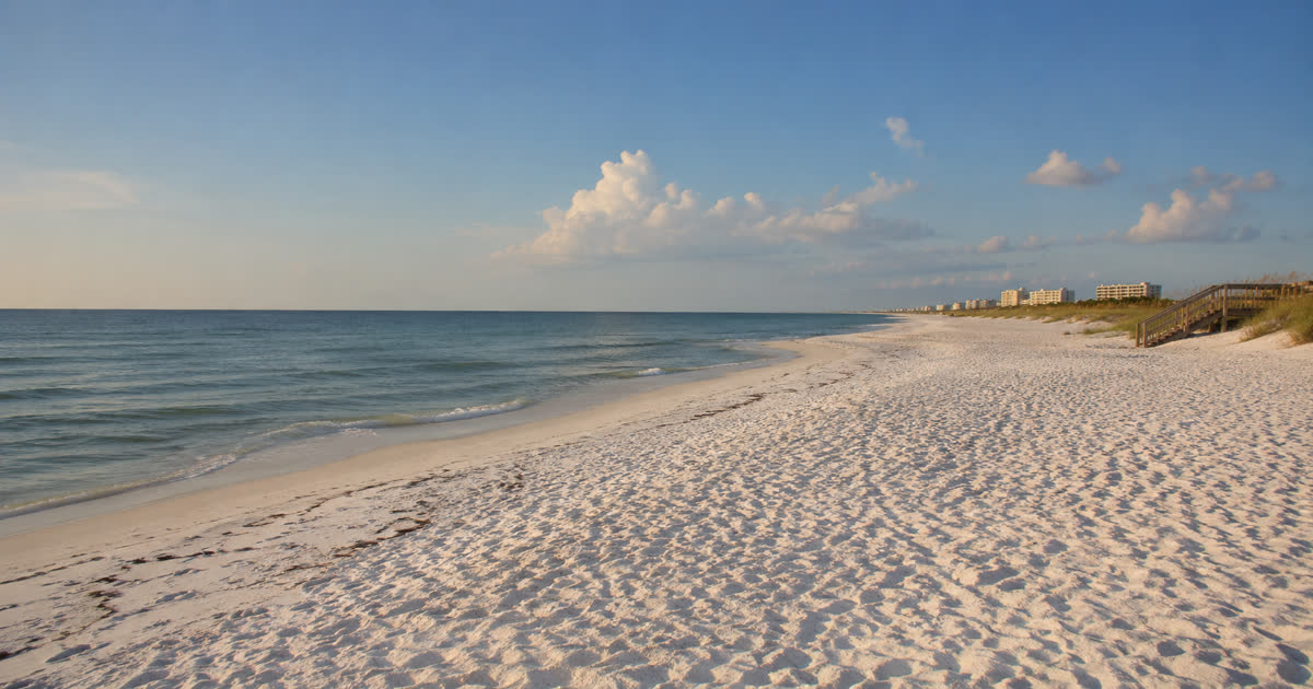 White sand beach at Gulf Shores, Alabama with calm green Gulf water and a clear sky